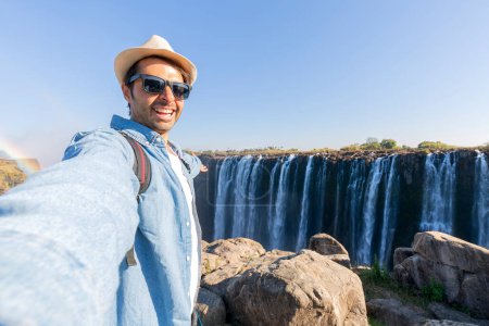 Tourist with a backpack at the Victoria Falls on Zambezi River located at the border of Zambia and Zimbabwe, the largest waterfall in the world.
