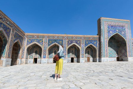 Glückliche attraktive Touristin mit Hut posiert am Eingang des Registan-Platzes in Samarkand, Usbekistan