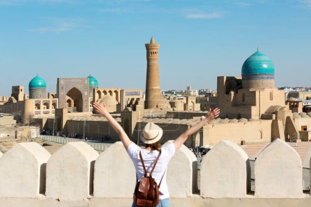 Téléchargez les photos : Vue panoramique de Boukhara, jeune touriste avec les bras levés devant la ville de Boukhara - Ouzbékistan - en image libre de droit
