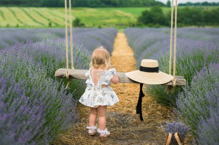 Téléchargez les photos : Une belle petite fille marche dans un champ de lavande. La blonde sourit et joue. champ de lavande - en image libre de droit
