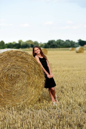 Téléchargez les photos : Jeune fille près de la meule de foin sur un champ récolté - en image libre de droit