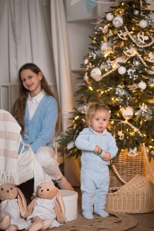Téléchargez les photos : Deux belles filles jouent près du sapin de Noël. Les sœurs célèbrent Noël. - en image libre de droit