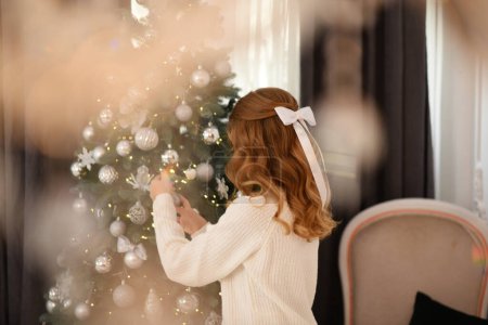 Foto de Hermosa joven con el pelo largo cerca del árbol de Navidad. Vacaciones de Navidad en casa - Imagen libre de derechos