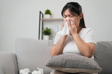 Une jeune femme a eu une allergie nasale éternuant assis sur le canapé à la maison. Grippe, grippe, maladie, fièvre, maladie. Soins de santé et concept médical.
