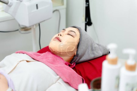 Photo for Beautiful young Asian woman getting a facial mask treatment at the beauty salon. Facial skincare. Beauty skin care. - Royalty Free Image