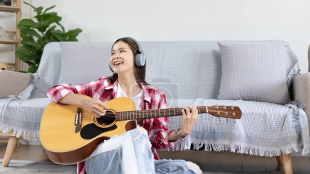 Asian female artist playing the guitar and singing happily in the living room, Relaxation with music therapy, Spending free time with music, Joy of playing music, Acoustic guitar.