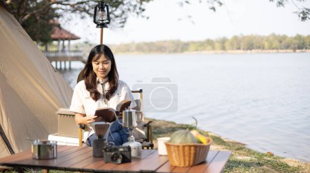 Foto de Young woman camping for the weekend in the woods near the river, Enjoying Camping Holiday In Countryside, woman sitting and relaxing happily reading definitions, Young woman outdoor leisure activities. - Imagen libre de derechos