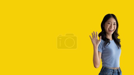 Téléchargez les photos : Waving hand in hi, Asian woman smiling friendly greeting, Hello,nice to meet you,say hi, Say hi and greet you, Welcome new people Join a multicultural team, Goodbye, Isolated on yellow background. - en image libre de droit