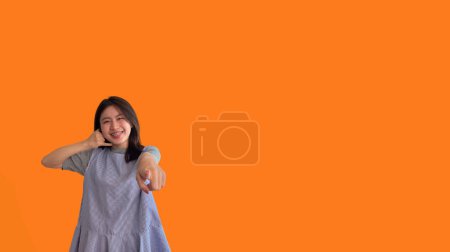 Foto de Señal de llamada, Mujer asiática joven brillante invitando a llamar aislado en fondo naranja, Sugiera llamar o invitar a solicitar la membresía, Aislado en fondo naranja - Imagen libre de derechos
