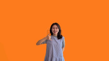 Foto de Señal de llamada, Mujer asiática joven brillante invitando a llamar aislado en fondo naranja, Sugiera llamar o invitar a solicitar la membresía, Aislado en fondo naranja - Imagen libre de derechos