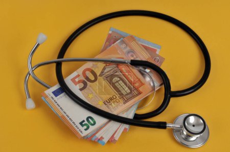 Foto de Stethoscope with a wad of euro banknote close-up on a yellow background - Imagen libre de derechos