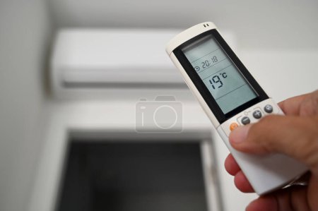 Photo for Adjusting the air conditioning with a remote control in hand - Royalty Free Image