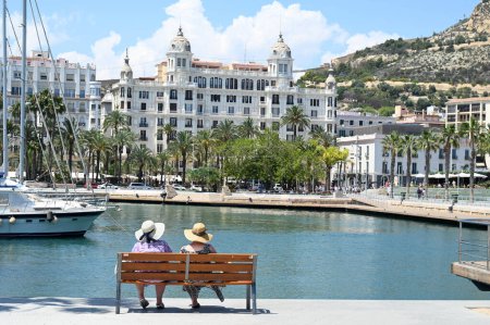 Foto de Dos mujeres sentadas en un banco frente al puerto deportivo de Alicante y la Casa Carbonell - Imagen libre de derechos