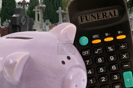 Foto de Concepto de gastos funerarios con una calculadora y una alcancía con un cementerio al fondo - Imagen libre de derechos