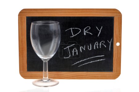 Foto de Concepto de enero seco con una pizarra escolar y una copa de vino vacía sobre fondo blanco - Imagen libre de derechos