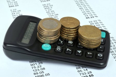 Photo for Stacks of Euro coins placed on a calculator with a list of numbers in the background - Royalty Free Image