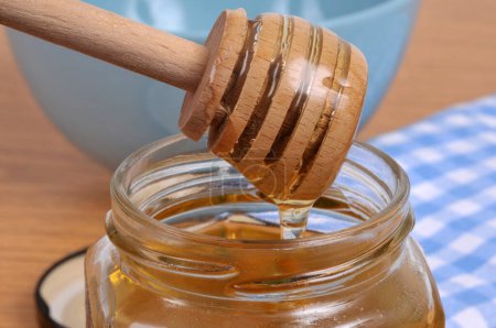Foto de Miel líquida que fluye de una cuchara de miel de madera en una olla de miel - Imagen libre de derechos