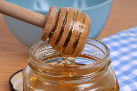 Foto de Miel líquida que fluye de una cuchara de miel de madera en una olla de miel - Imagen libre de derechos