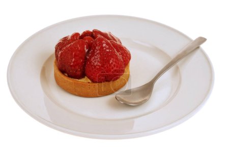 Strawberry tartlet in a plate with a spoon closeup isolated on a white background