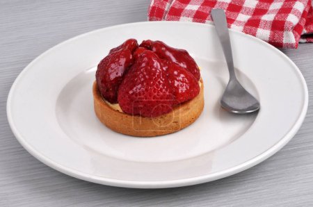 Strawberry tartlet on a plate with a spoon close-up