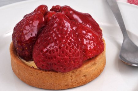 Strawberry tartlet on a plate with a spoon close-up