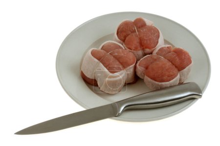 Tres paupiettes de ternera cruda en un plato con un cuchillo de cerca sobre un fondo blanco 