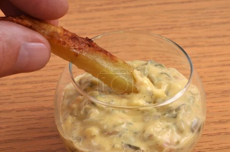 Dip a fries in a ramekin of bearnaise sauce closeup on wooden background