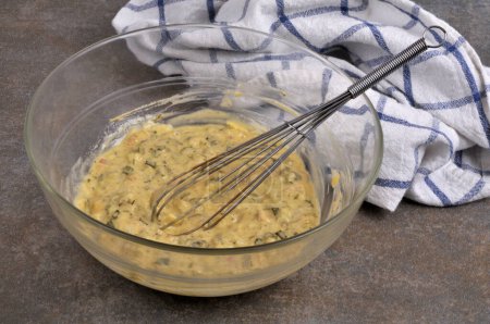 Salad bowl of homemade bearnaise sauce with a kitchen whisk and a tea towel close-up on a gray background 