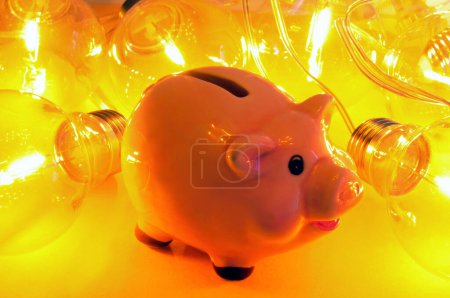 Electricity expenses concept with a piggy bank and a garland of electric bulbs on a yellow background 