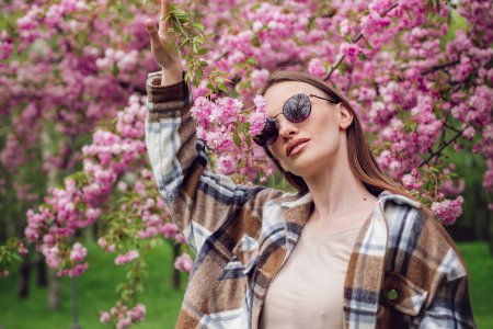 Téléchargez les photos : Portrait de charmante femme à la mode dans le parc sakura en fleurs - en image libre de droit
