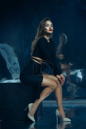 Foto de Sexy dama de moda en vestido negro posando en el estudio sobre fondo de lámina oscura - Imagen libre de derechos