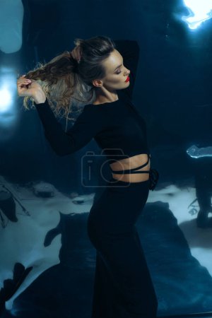 Foto de Sexy dama de moda en vestido negro posando en el estudio sobre fondo de lámina oscura - Imagen libre de derechos