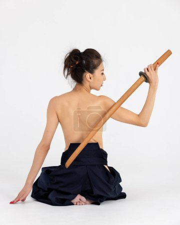 Téléchargez les photos : Maître de l'Aïkido femme en kimono samouraï traditionnel hakama avec ceinture noire avec épée en bois bokken, katana sur fond blanc. Style de vie sain et concept sportif. - en image libre de droit