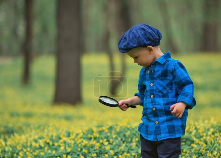 Téléchargez les photos : Joyeux petit garçon heureux, explorant la nature avec une loupe, l'été. Concept de l'enfant et de la nature - en image libre de droit