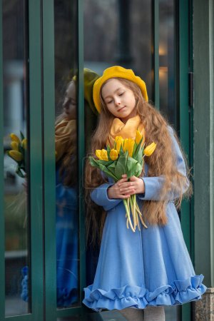 Téléchargez les photos : Portrait d'une fille heureuse avec un bouquet de tulipes jaunes lors d'une promenade au printemps. Fleurs pour la Journée internationale de la femme. Le concept de beauté, d'amour, de printemps et d'enfance - en image libre de droit