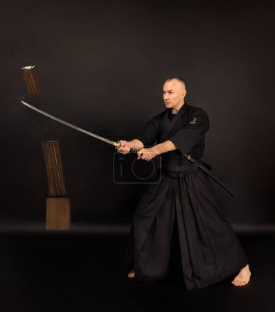 Foto de Retrato de aikido sensei master con cinturón sensei negro en taekwondo kimono witn sword katana sobre fondo negro. Tradicional samurai hakama kimono. Estilo de vida saludable y concepto deportivo. - Imagen libre de derechos