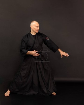 Foto de Retrato de maestro sensei aikido con cinturón sensei negro en kimono taekwondo sobre fondo negro. Tradicional samurai hakama kimono. Estilo de vida saludable y concepto deportivo. - Imagen libre de derechos