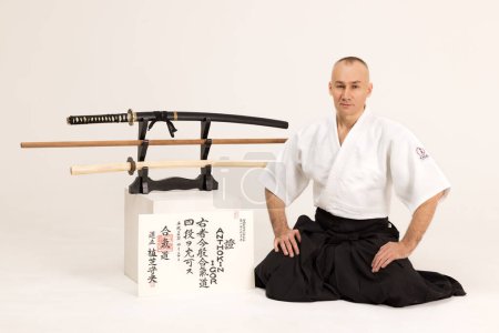 Téléchargez les photos : Portrait de maître aikido sensei avec ceinture sensei noire en taekwondo kimono witn sword katana sur fond noir. Kimono samouraï traditionnel hakama. Style de vie sain et concept sportif. - en image libre de droit