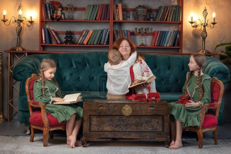 Téléchargez les photos : Bonne grand-mère et petits-enfants lire le livre ensemble et s'amuser à la maison - en image libre de droit