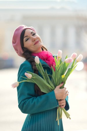 Photo for Beautiful woman with spring tulips flowers bouquet at city street. Happy portrait of girl smiling and holding pink tulip flowers outdoors on 8 march - Royalty Free Image
