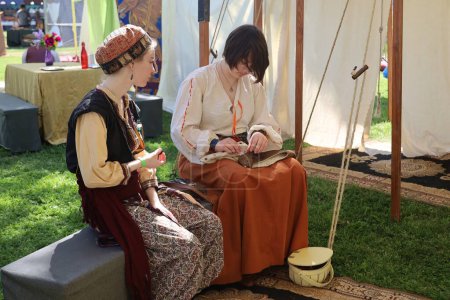 Photo for 4-15-2023: Visalia, California: Women in period costumes at a Renaissance Faire, sewing - Royalty Free Image