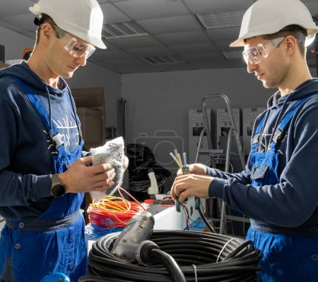 Photo for Technicians work with cables for installing into plugs for charging electric cars on station. Electricians examine quality of cables and establish into charger - Royalty Free Image