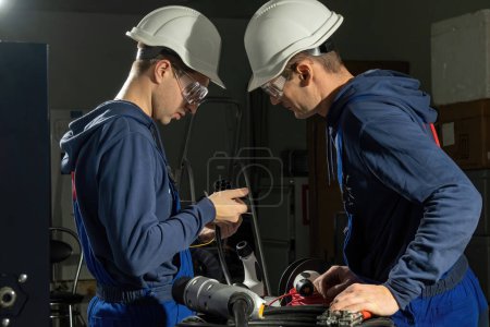 Photo for Electricians check charging plug with repaired cables in workshop. Technicians wearing hardhats check quality of charger for electric car - Royalty Free Image