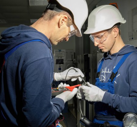 Foto de Los electricistas trabajan en un laboratorio equipado con enchufe de carga y voltaje de comprobación con el probador. Los técnicos instalan cables en el conector para cargar EV - Imagen libre de derechos