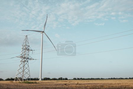 Téléchargez les photos : Une éolienne écologique produit de l'énergie propre. Moulin à vent génère de l'énergie renouvelable pour soutenir la ligne de transport d'énergie contre la tour sous le ciel - en image libre de droit