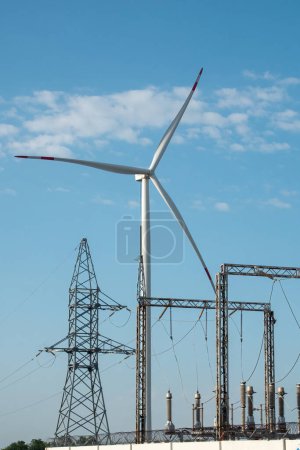Foto de Molino de viento produce energía renovable. La turbina eólica genera energía contra la subestación de distribución de electricidad bajo cielo azul - Imagen libre de derechos