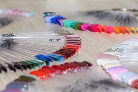 Téléchargez les photos : Conseils pour montrer différentes nuances de gel vernis à ongles de couleur se trouvent sur la table en bois. Échantillons en forme de ventilateur pour la conception de manucure en gros plan salon - en image libre de droit