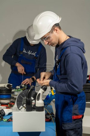 Photo for Workers tries to install cables into plug for charging electric car in special equipped laboratory. Technicians wearing helmets works with cables - Royalty Free Image
