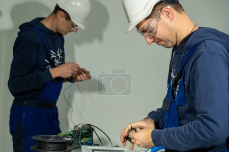 Foto de Los electricistas trabajan con la placa base e instalan cables para un correcto funcionamiento. Técnicos sueldan cables en la placa base para instalar en enchufes - Imagen libre de derechos