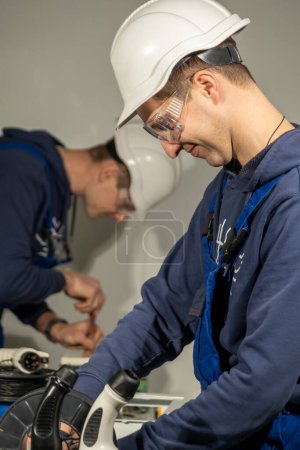 Photo for Electrician enjoys working in equipped workshop with important details for making charger. Technician repairs plug for charging EV on stations - Royalty Free Image